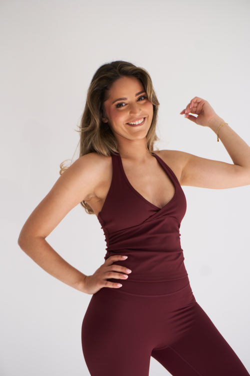 A woman posing in a matching burgundy halter top and high-waisted leggings set against a plain white studio background.